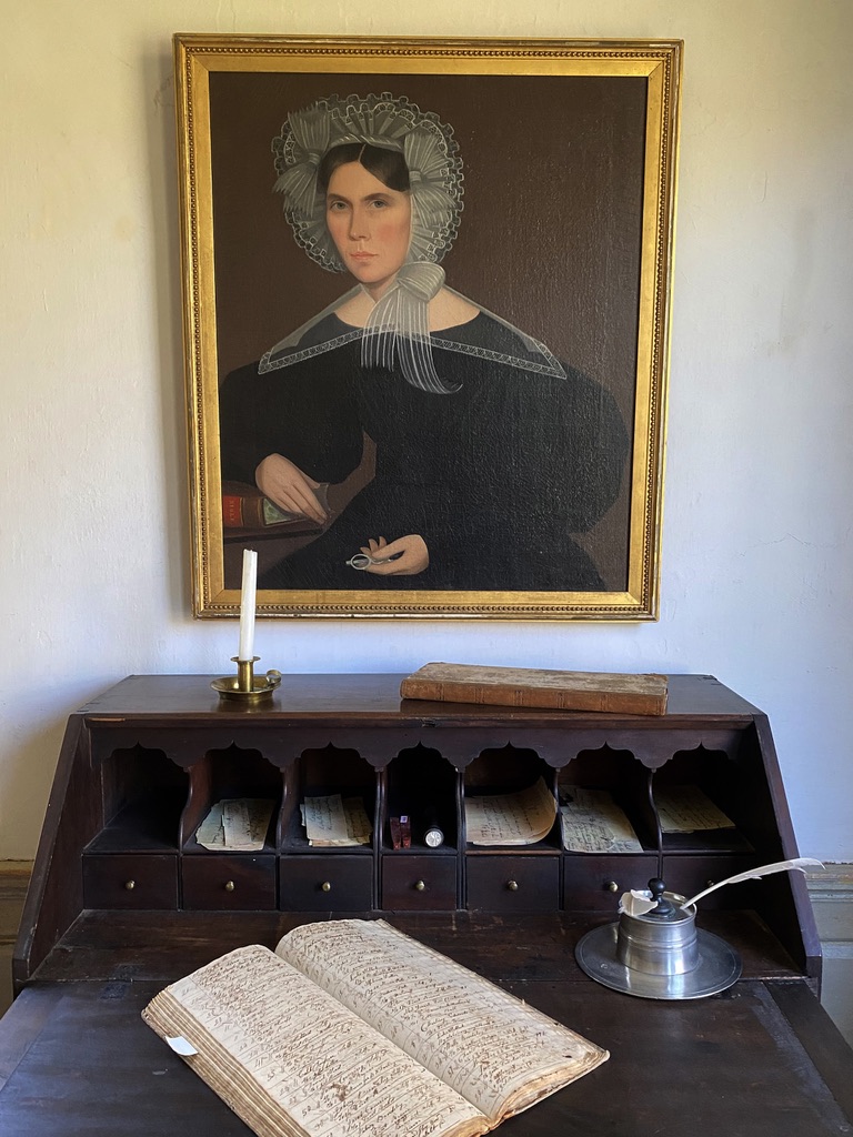 Antique writing desk with an oil painting hanging on the wall above.